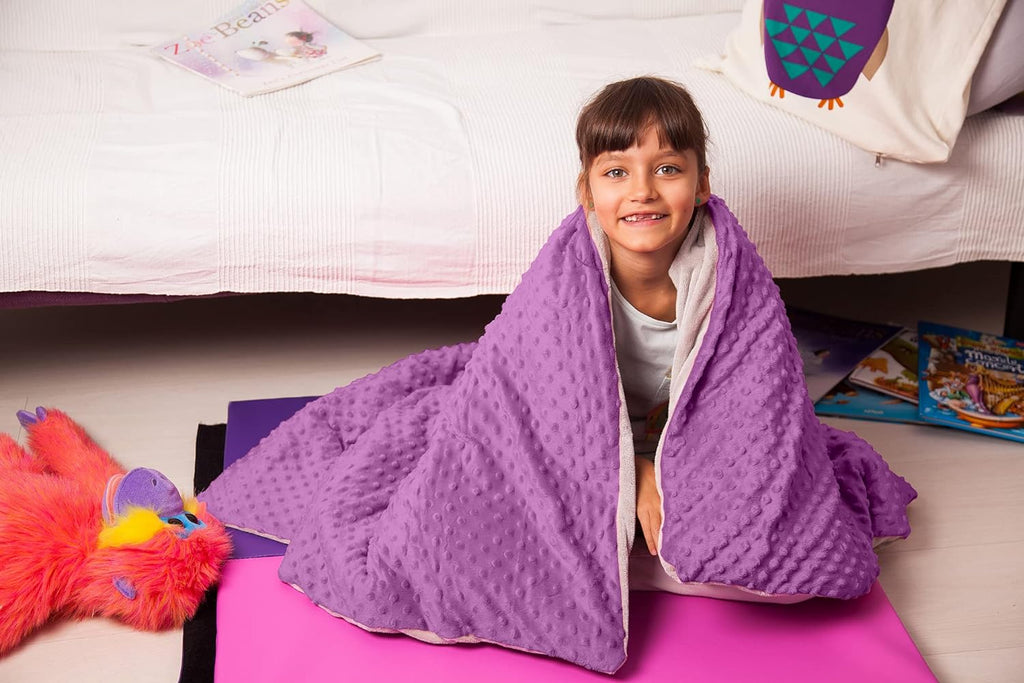 Child wrapped in a soft purple textured Blue Dream 7lb Kids Weighted Blanket | Calming Sensory Blanket for Ages 5–10 sitting on a pink mat in a cozy bedroom setting