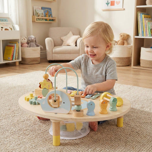 A toddler playing happily with the 7-in-1 Montessori Activity Table | Wooden Musical Sensory Play Table for 12 Months+ in a cozy, well-lit room with toys and bookshelves.