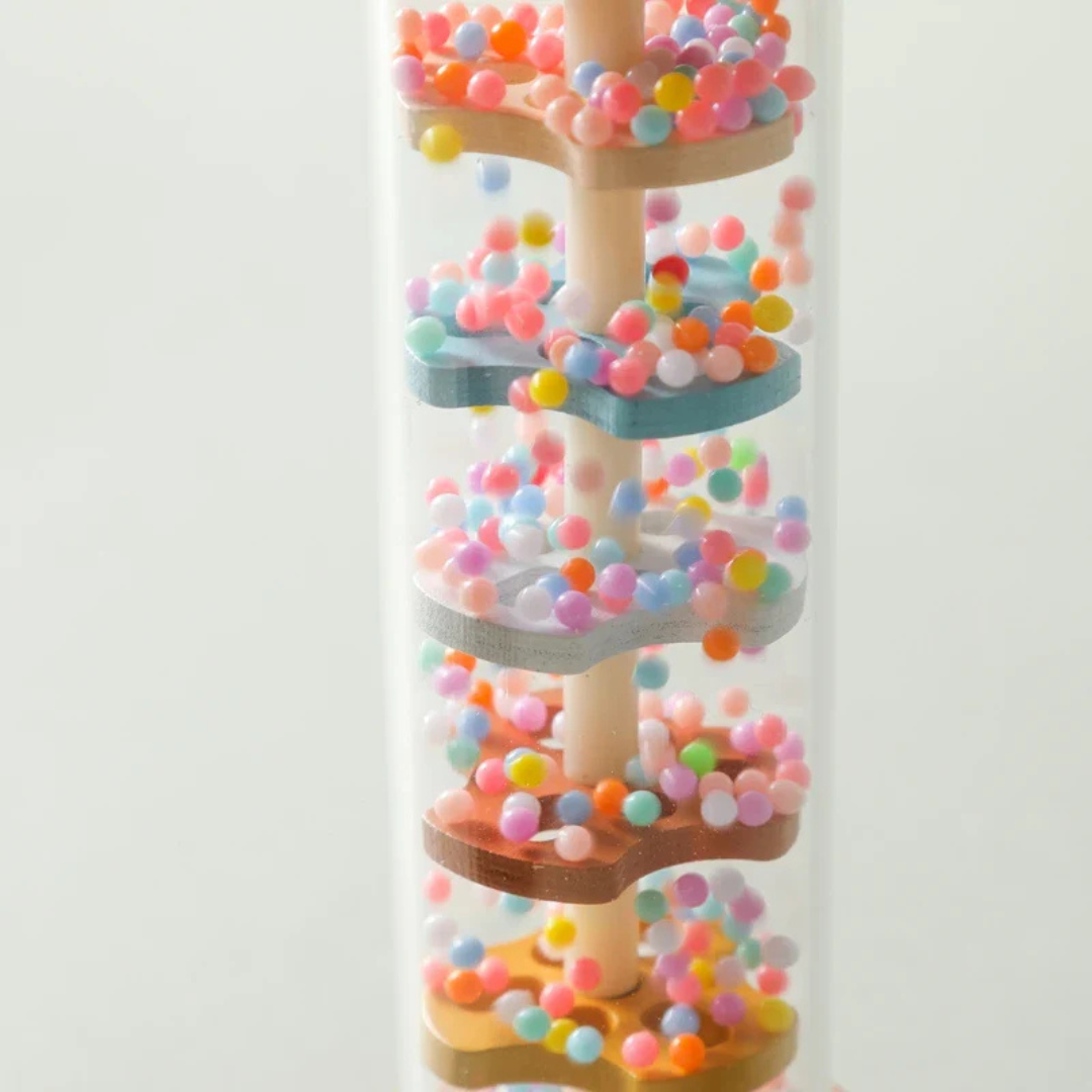 Clear close-up of a Montessori Wooden Rain Stick Rattle Toy with colorful beads moving around wooden flower-shaped platforms inside a transparent tube, designed for sensory play.