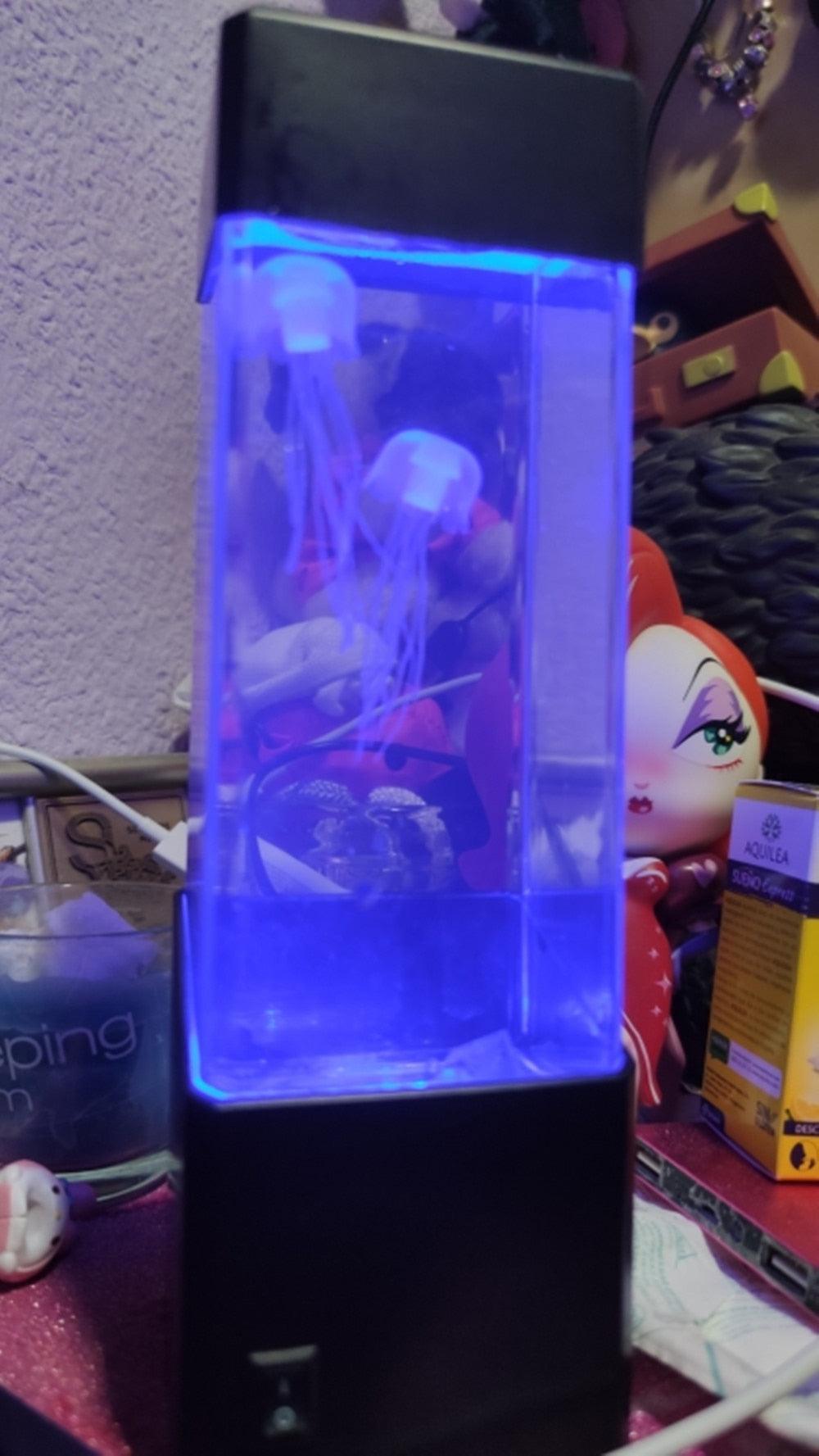 LED Jellyfish Sensory Lamp | Calming Visual Night Light for Autism & ADHD emitting a soothing blue glow with floating jellyfish inside a clear tank on a cluttered desk.